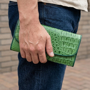 Cartera con solapa de piel de cocodrilo verde, sostenida junto a tela vaquera oscura
