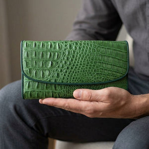 Cartera larga de tres pliegues de piel de cocodrilo verde, sostenida con naturalidad en una mano adulta