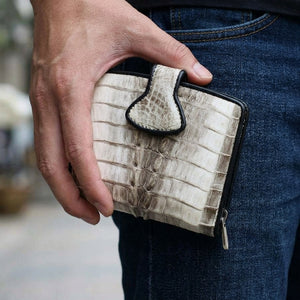 Cartera de cuero de cola de cocodrilo gris y blanca sostenida junto a tela vaquera oscura