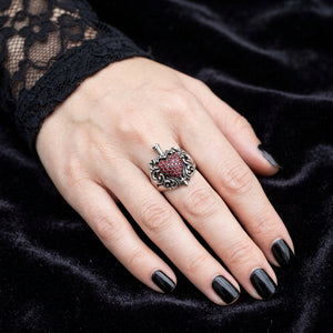Zilveren ring met rood hart en dolk gedragen aan de vinger van een vrouw met zwarte nagels en een gotische kanten manchet