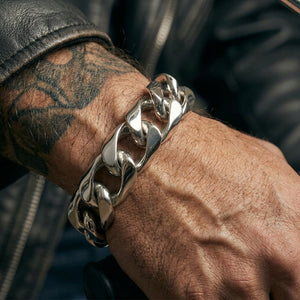 Heavy curb-link sterling silver bracelet worn on a tattooed wrist beside a black leather sleeve