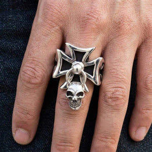 Zilveren ring met zwart ijzeren kruis en bungelende schedel, gedragen om een mannenhand