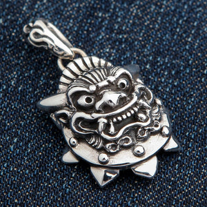 Colgante de máscara de demonio japonés en plata de ley mostrando la máscara sobre tela vaquera