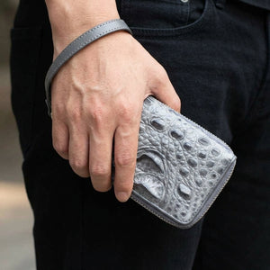 Cartera de piel de cocodrilo gris claro con doble cremallera sostenida junto a la cadera