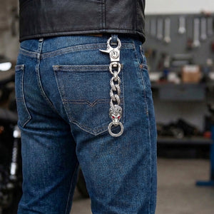 Red-eye silver lion keychain clipped around a rear jeans belt loop beneath a black leather jacket, showing three flame links and the lower key ring.