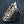 Three-quarter close-up on denim, the dagger raised down the center of a sterling silver shield cut with scrollwork.
