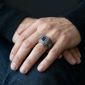 Hands resting on dark denim, wearing a 1952 Michigan State silver championship ring with a blue stone.