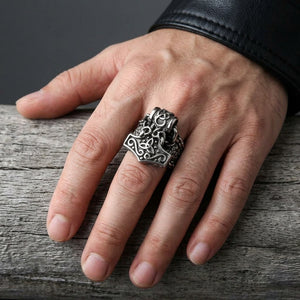 Mjölnir-Charm-Ring aus Sterlingsilber mit schuppenstrukturierter Schiene und Triqueta-Details, getragen an einem erwachsenen Mittelfinger über verwittertem grauem Holz.