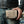 Cream and black natural snakeskin trifold held horizontally beside a leather jacket and jeans, with braided edging and two flame snaps visible.