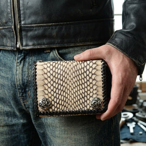 Cream and black natural snakeskin trifold held horizontally beside a leather jacket and jeans, with braided edging and two flame snaps visible.