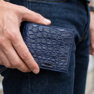 Cartera de piel de vientre de cocodrilo azul marino sostenida junto a tela vaquera oscura