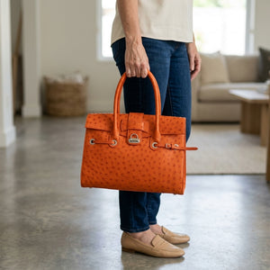 Orange Ostrich Leather Handbag carried by its handles beside the hip