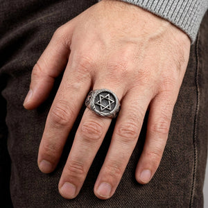 Sølvsignetring med Davidsstjerne og ouroboros båret på en hånd over brun denim.