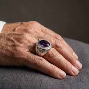 Oval amethyst sterling silver bishop ring worn on a hand against a neutral background
