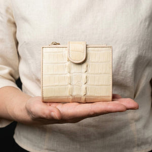 Cartera con broche de presión de cola de cocodrilo blanco perla sostenida por la mano de una mujer en plano medio corto, mostrando su lengüeta redondeada y escamas crema