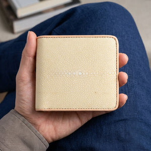 Pearl-white stingray bifold with tan edging held over a navy-clothed lap.