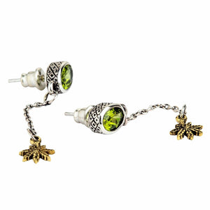 Orecchini pendenti in argento sterling 925 con peridoto e foglia d'oro. Gli orecchini poggiano inclinati, mostrando i castoni delle pietre verdi, i perni e le piccole foglie color oro.
