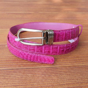 Pink crocodile leather women's belt with silver buckle coiled on wooden surface