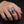 Adult hand wearing the R2586 sterling silver skull ring with a 14K yellow gold cross on a charcoal background
