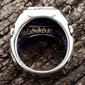 Rückansicht durch die Ringschiene aus Sterlingsilber auf Baumrinde, wobei die Unterseite des blauen Steins durch die Fassung sichtbar ist