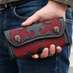 Cartera tríptico con cruz tribal de piel de raya roja y negra sostenida junto a la cadera