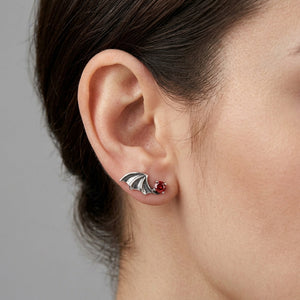 Orecchino a lobo ala di pipistrello in argento con zirconia cubica rossa su un lobo scoperto, accanto a capelli castani pettinati all'indietro, in un profilo laterale naturale.