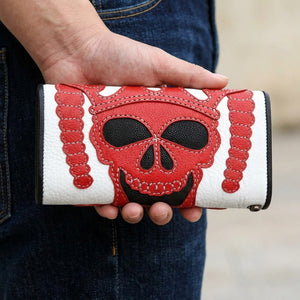 Cartera cerrada de piel de raya con calavera de diablo roja sostenida en una mano contra tela vaquera oscura