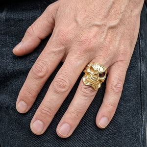 Gold-color skull ring with dark red eye stone worn on a natural adult hand