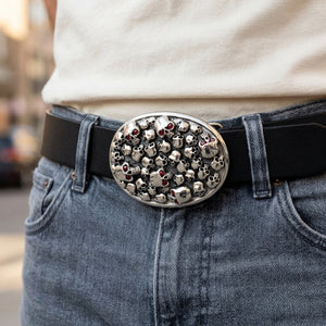 Oval silver skull-pile buckle with red eye accents worn on a styling belt over grey jeans.