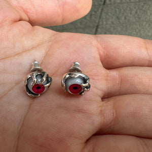 Pendientes de botón de plata de ley con ojo rojo, par de pendientes con ojo rojo vistos desde arriba en una mano
