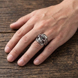 Bague tête de mort compacte en argent avec deux pierres oculaires rouge foncé portée sur une main détendue