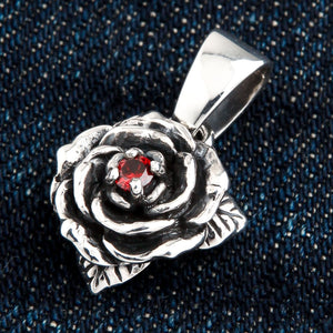 Ciondolo rosa con granato in argento sterling. La rosa è ruotata dall'altra parte su denim per mostrare i petali che circondano il granato.