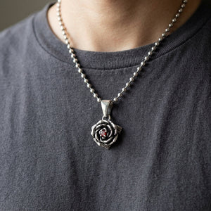 La rosa d'argento e il suo centro in granato rosso pendono da una catena di stile su una camicia color antracite.