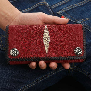 Red stingray trifold wallet supported in one hand, showing both silver snaps and the central pearl marking
