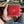 Red stingray bifold with tan leather trim supported in a hand above blue jeans, showing its small pale pearl cluster.