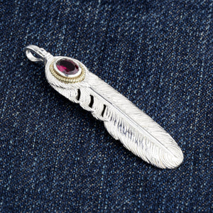 Vista diagonale del pendente a piuma con granato su denim, che mostra le fenditure aperte nel vessillo d'argento.