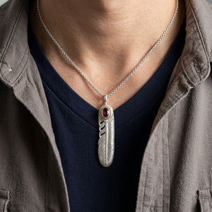 Pendente a piuma con granato rodolite su catena d'ambientazione sopra top blu navy e camicia grigia.