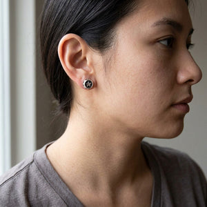 A round silver star stud is worn on an exposed adult earlobe above a grey shirt.