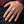 Silver cross ring with a dangling gold-tone skull worn on a relaxed hand beside a burgundy cuff.