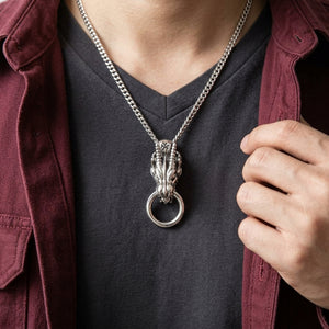 Ciondolo in argento a testa di drago con anello rotondo nella bocca su catena da styling sopra una camicia scura.