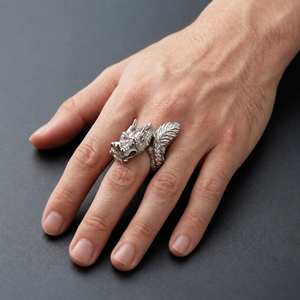 Silver sculptural dragon ring with horned head and featherlike tail worn on a hand