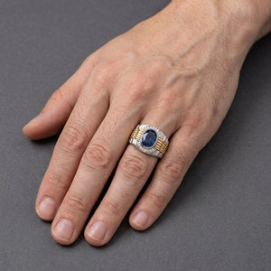 Silver and gold watch-band-style ring with oval blue CZ worn on a light-skinned hand