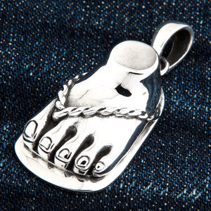 Sandaalvoet-hanger van 925 sterling zilver. De voet rust onder een naar links gerichte hoek op denim, waarbij de gepolijste tenen en het hangoog zichtbaar zijn.