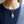 De zilveren sandaalvoet-hanger hangt aan een stylingketting tegen een marineblauwe geribde top.