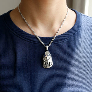 De zilveren sandaalvoet-hanger hangt aan een stylingketting tegen een marineblauwe geribde top.