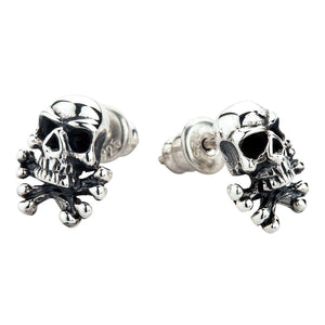 Totenkopf und gekreuzte Knochen Ohrstecker aus Sterlingsilber. Die Totenkopf-und-gekreuzte-Knochen-Ohrstecker weisen in entgegengesetzte Richtungen, wobei ihre Rückseiten dahinter sichtbar sind.