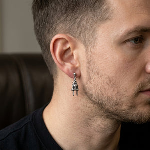Petite boucle d'oreille en argent en forme de prise électrique avec tête de mort portée à l'oreille d'un mannequin homme