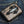 Grey snake trifold wallet laid diagonally on denim, with a black stingray cross and two flame snaps.