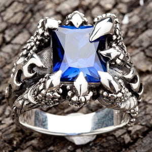 A gothic-style ring with monster talons holding a large blue sapphire, a piece of men's fantasy jewelry.