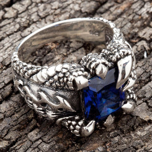 A heavy silver biker ring for men, designed with monstrous claws holding a large, square blue gemstone.